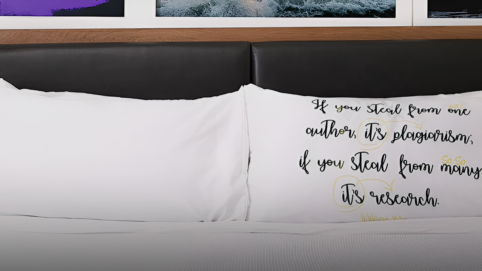 A neatly made bed with white pillows, black headboard, and art-filled wall. Two lamps glow on either side, a cozy, gallery-like bedroom.