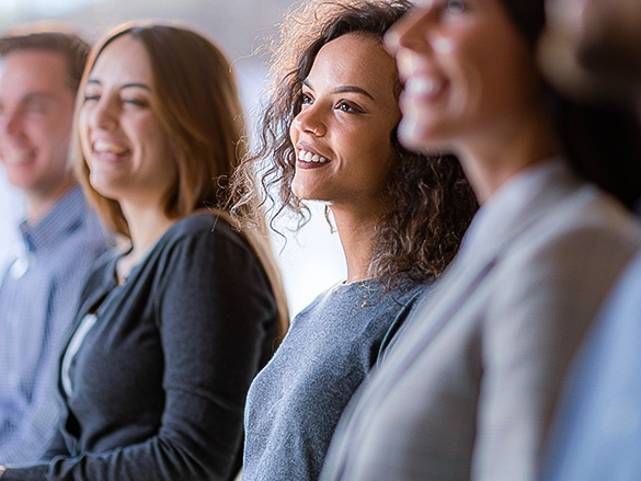 A group of diverse people sitting together, smiling and listening intently at an event or presentation.
