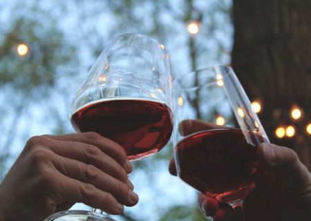 Two people clink glasses in a snowy outdoor setting, with warm drinks and festive mood. end with a period.