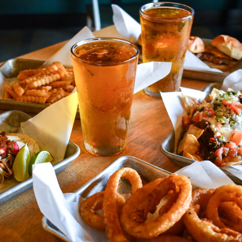 A table of Tex-M-Mex favorites: nachos, tacos, onion rings, salsa, and two iced teas, ready to share.
